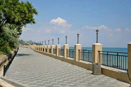 路堤。黑海。现代设计。人行道上铺满了路边的瓷砖。金属栅栏和照明灯。全景海是绿松石和蓝色。白云与蓝天