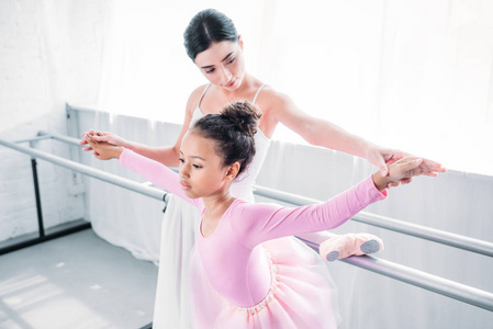 可爱的非洲裔美国儿童粉红色的芭蕾舞短裙与教师在芭蕾学校锻炼