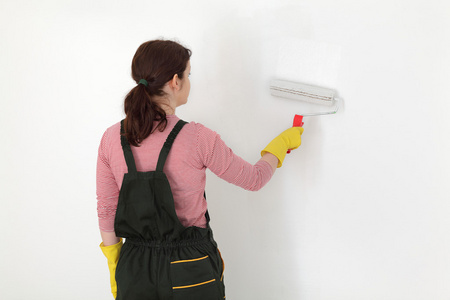 年轻的工人粉刷墙壁为白色的房间里照片