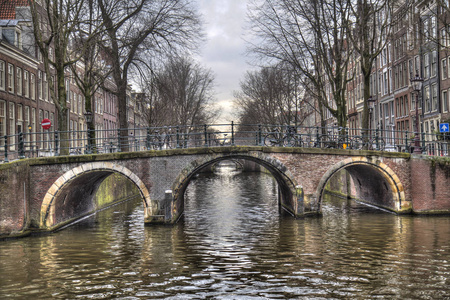 运河和桥梁在历史上阿姆斯特丹, 荷兰与停放的自行车和汽车和树在冬天