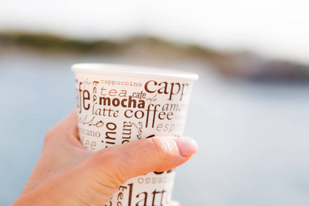一只女性手捧着一杯咖啡在海前, 美丽的景色