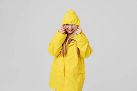 穿着黄色雨衣的金发女郎, 头上有个头巾, 在灰色的背景下躲在雨中。