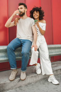 全长视图时尚的年轻人种情侣喝咖啡从纸杯在街上