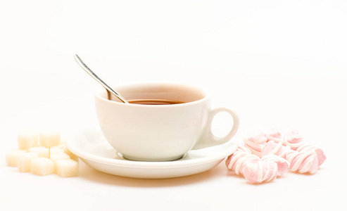 杯子里有红茶和糖果。杯子里装满了黑色酿造的茶叶, 勺子和一堆棉花糖和精制糖的白色背景。茶歇概念。甜点准备的饮料和甜点