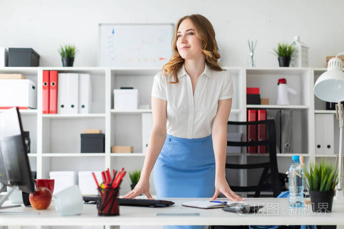一个漂亮的年轻女孩站在办公室里, 手放在桌子上.