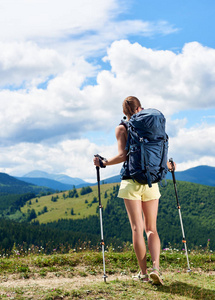后视图的运动女子徒步旅行在一条山小径, 走在草地上, 穿着背包, 使用徒步棍, 享受夏日阳光明媚的一天在山上。旅游理念
