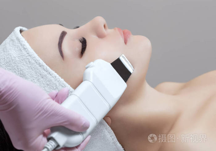 医生美容师使该仪器的一个程序, 超声波清洗面部皮肤的美丽, 年轻女子
