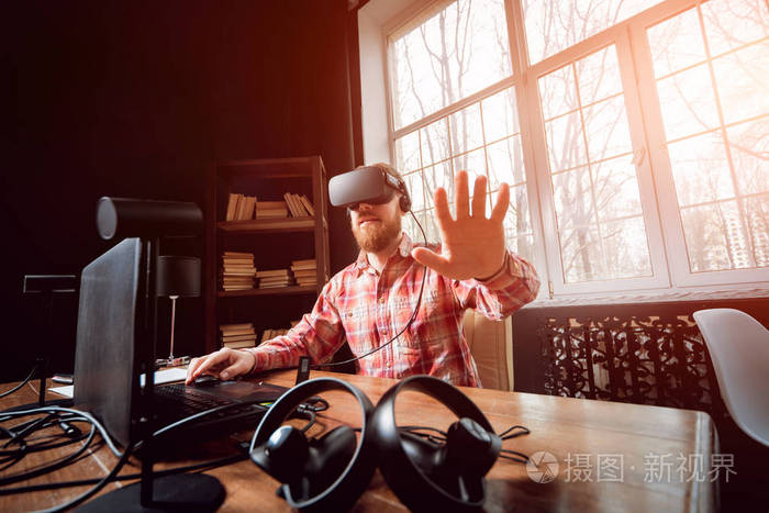 年轻的胡子男子戴着虚拟现实护目镜在办公室