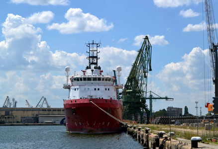 一艘大型的红白海货船停泊在港口, 前视。还有一些港口起重机和技术大厦