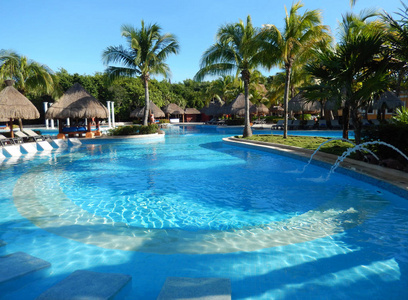 游泳池坐的区域与稻草伞, 贵妃椅和棕榈树景观, 在加勒比海海滩度假村在海滨玛雅, 在坎昆, 墨西哥