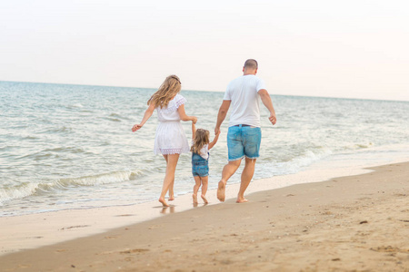 关闭幸福的家庭三美丽的妻子, 父亲和女儿在海滩上漫步在日落的乐趣。家庭旅游概念。夏日