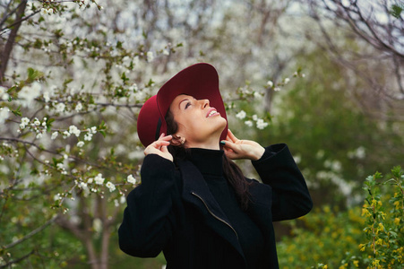 年轻漂亮的时髦女人，戴着帽子的画像。一棵开花的树旁摆姿势。女性的美丽和时尚