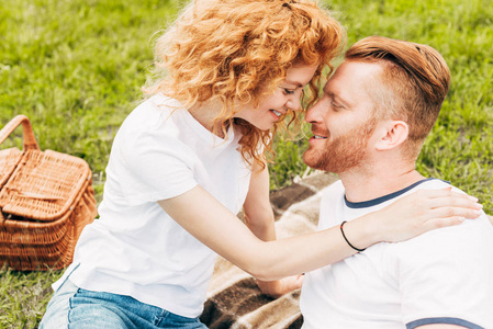 愉快的红发夫妇在公园野餐一起微笑的侧面视图