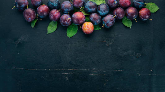 新鲜李子与叶子。水果。在黑色的木质背景。顶部视图。文本的可用空间