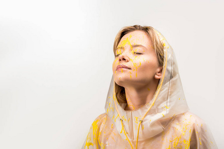 美丽的妇女在雨衣画与黄色油漆站在白色的紧闭的眼睛