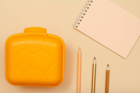 学校用品。笔记本, 彩色铅笔和在米色背景的午餐盒。具有复制空间的顶部视图。回到学校的概念。粉彩色