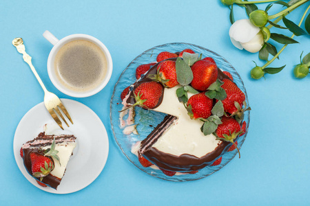 自制巧克力蛋糕, 用新鲜的草莓和薄荷的叶子装饰在玻璃盘子上, 一块蛋糕配上白色盘子上的叉子, 一杯咖啡, 还有在蓝色背景上的牡丹
