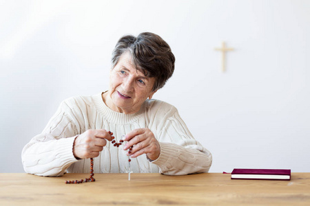 微笑的宗教祖母与念珠坐在桌子上与圣经