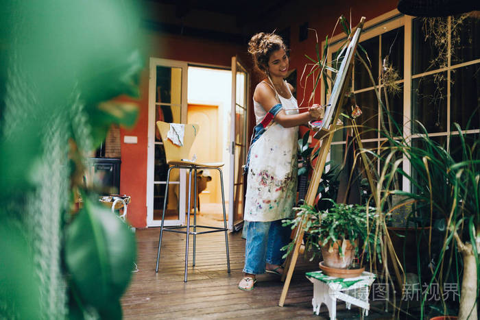 室内镜头的专业微笑女画家画在帆布在工作室与植物