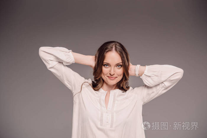 在灰色背景下的头部被隔绝的微笑的有吸引力的妇女摆在头后面照片