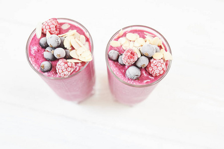 两杯粉红色水果奶昔或冰沙或鸡尾酒在白色木质背景。健康的多汁维生素饮料饮食或纯素食的食物概念