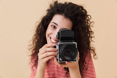 漂亮的年轻的卷发女摄影师的形象, 在米色背景持有相机隔离