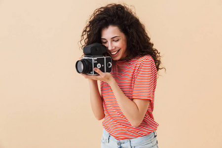 照片的美丽年轻的卷发女摄影师隔离在米色背景持有摄像头