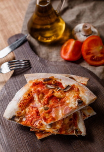 用火腿芝士蘑菇和番茄酱在木制的切板上切片比萨饼。顶部视图