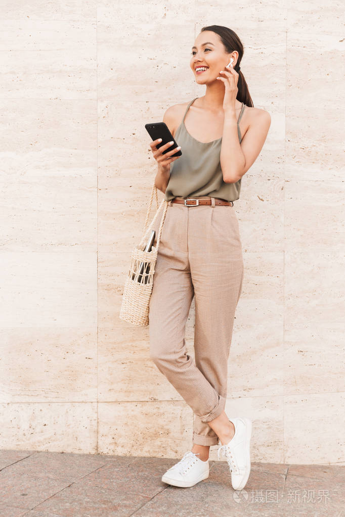 身穿休闲夏季服装的白种黑发妇女的形象触摸蓝牙 earpod 和手持手机