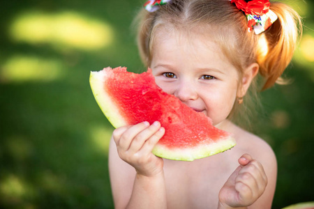 一个年轻的金发小女孩的肖像与西瓜, 夏季户外健康小吃的儿童。小女孩在花园里捧着一片西瓜