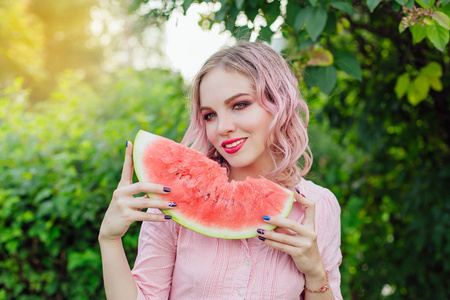 美丽的年轻女子，与粉红色的头发，享受甜甜多汁的西瓜