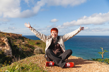 快乐的宽微笑红发女人坐在岩石上的沙滩上。戈佐岛, 马耳他