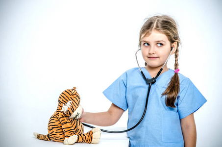 一个穿着手术服的小女孩听她与 phonendoscope 的玩具老虎