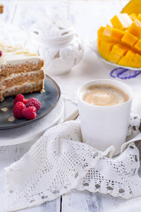 早餐用白奶油切蛋糕。芒果果。白色背景, 桌布与花边, 一杯咖啡和免费的文本或广告空间