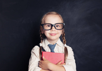 微笑的孩子女孩与书在黑板背景与拷贝空间。戴眼镜的小女孩。返回学校概念