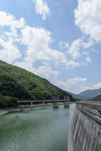 在西班牙的北美上空, 一座大坝的墙和后部建筑位于绿色水域附近的一个小山上。