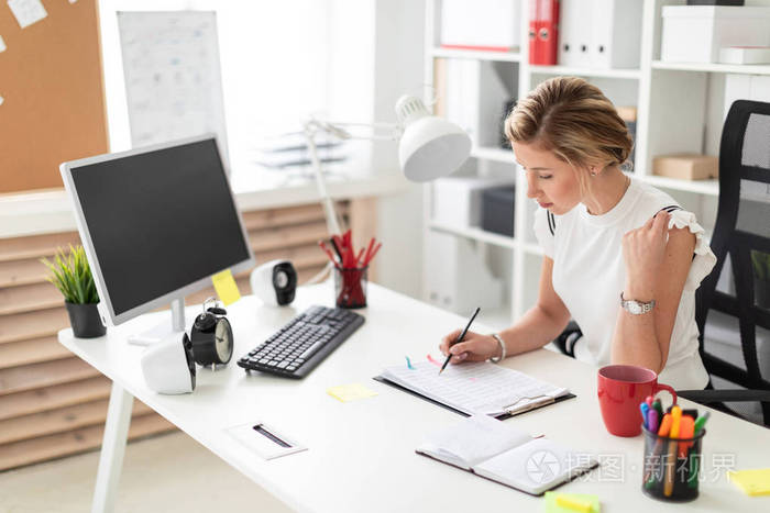 一个年轻的金发女郎坐在办公室的电脑桌前, 在文档里写了一支铅笔.