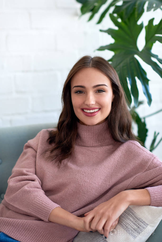 年轻自信的女人的肖像微笑着, 坐在沙发上看着相机