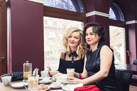 两个时髦的女孩坐在餐桌上的咖啡馆和饮料