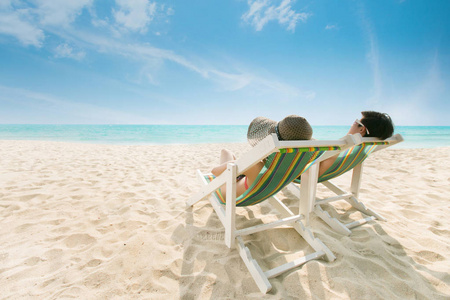 夫妇在沙滩椅上海滩上晒日光浴是明亮的蓝色。Dur