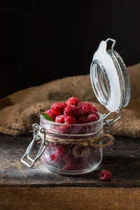 树莓在一个玻璃罐子在黑暗的木质背景。覆盆子背景。健康食品概念。新鲜有机浆果
