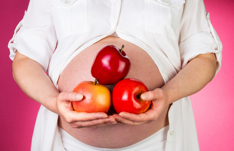 怀孕的女人苹果坚持粉红色背景