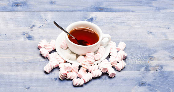 茶杯蘸泡茶和棉花糖。饮料酿造过程在杯子。茶歇概念。杯装黑色酿造茶, 勺子和棉花糖堆在木质背景