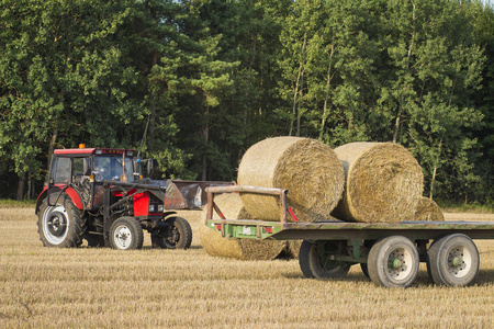 拖拉机把一捆干草装在拖车上。粮食作物收获后的田间农业机械
