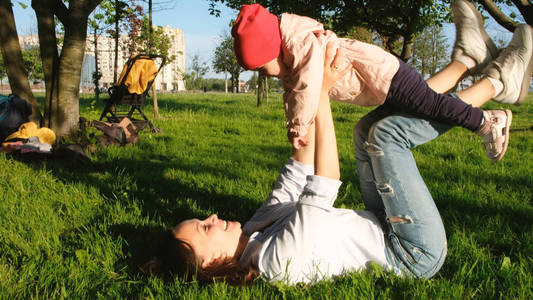躺了下来妈妈和躺在草地上, 妈妈正在日落的公园里和她的孩子玩耍.