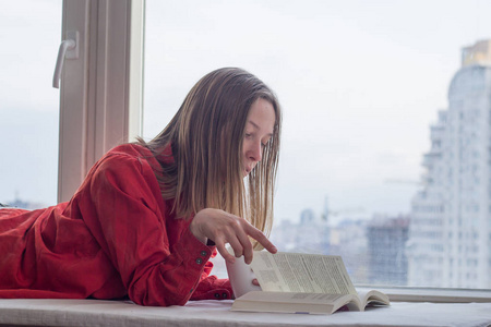 在窗台上用书和杯咖啡或茶 relzxing 的年轻女子画像