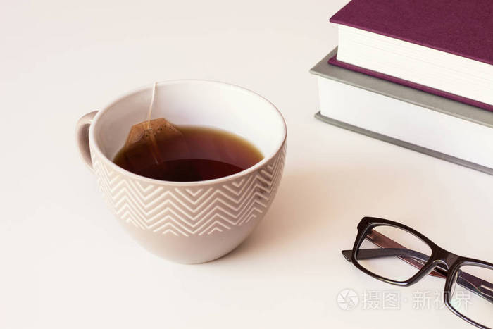 棕色陶瓷杯红茶和茶纸袋, 阅读眼镜与桌子上的书