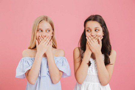 两个可爱的女孩的形象810 穿着衣服覆盖 mouthes 的手, 并期待彼此孤立的粉红色背景