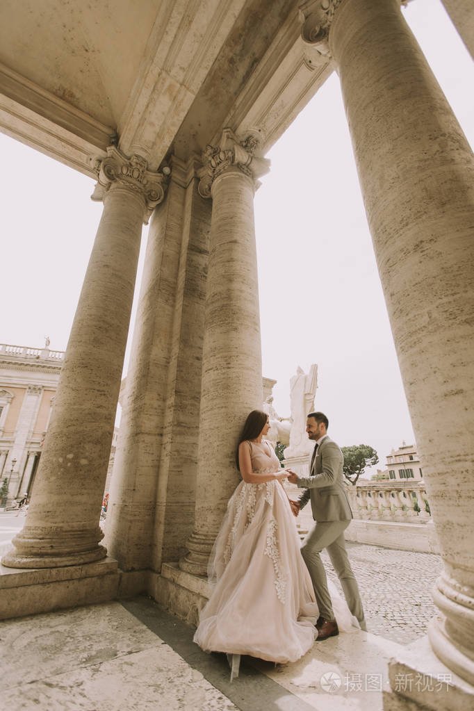 年轻迷人的新婚夫妇摆在罗马与美丽和古老的建筑背景