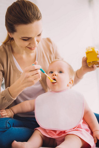 细心的母亲在给女儿喂食婴儿食品时微笑